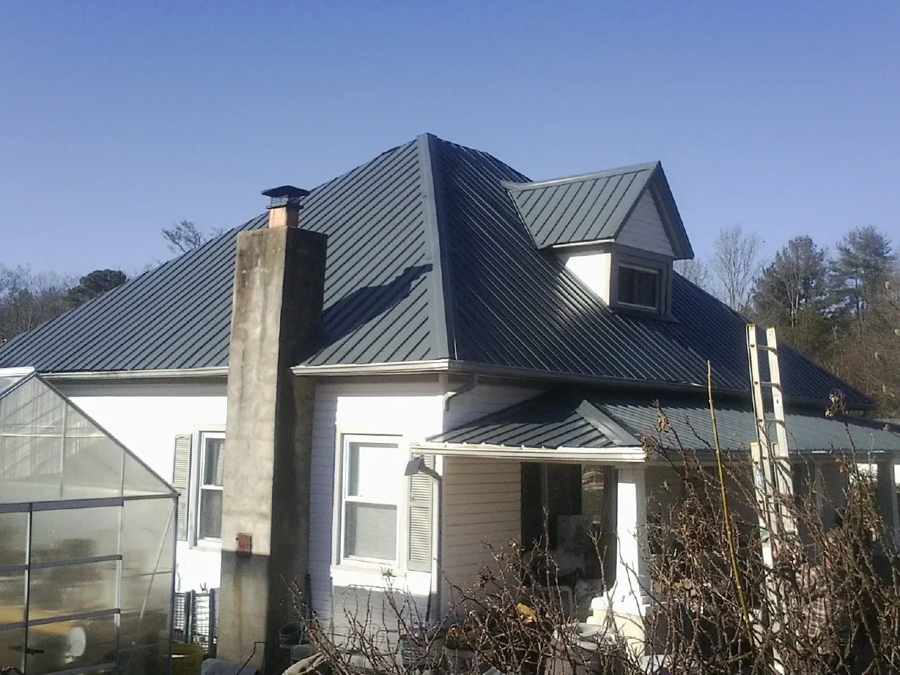 Dark blue standing seam metal roof on a white farmhouse with dormer — Slate & Tile Roof Repair by Roofing Brothers in Lombard