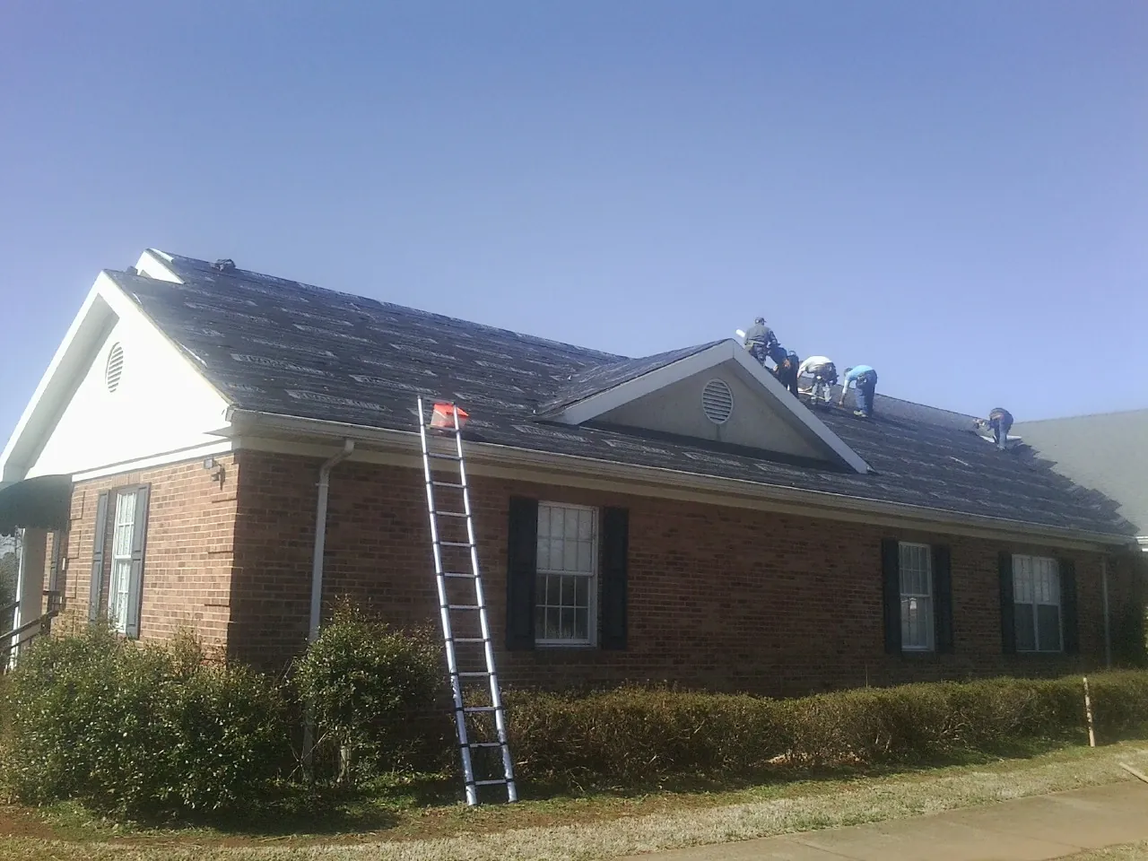 Crew tearing shingles off a brick ranch roof with a ladder set — Emergency Roof Repair work by our crew in Lombard