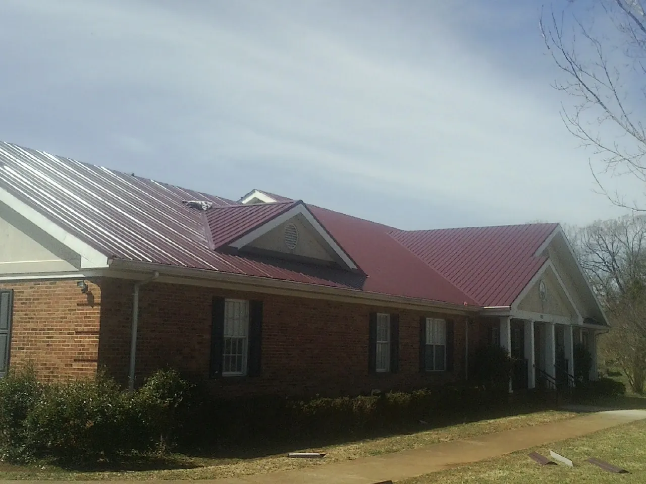 Red metal roof with gabled entries on a long brick building, from a Hail Damage Roof Repair job in Lombard
