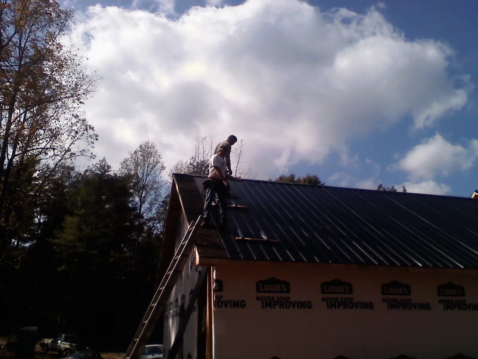 Roofer fastening dark metal panels high against a cloudy sky, from a Roof Inspection job in Lombard