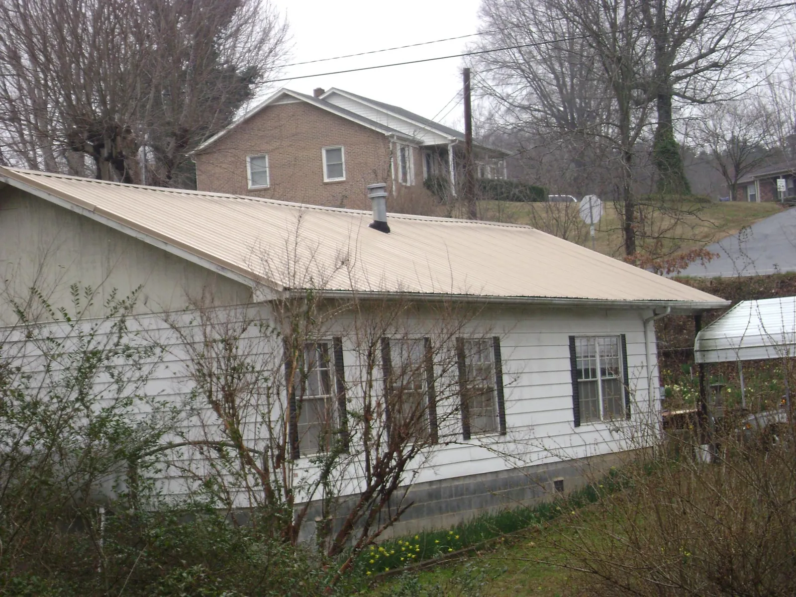 Tan metal roof on a white sided house set into a hillside — Commercial Roofing by Roofing Brothers in Lombard